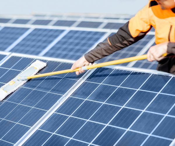 Workman cleaning solar panels Professional cleaner in protective workwear cleaning solar panels with a mob. Concept of solar power plant cleaning service