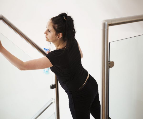 Woman standing on a staircase, cleaning a glass pane and banister rail.,Barnsley House,England Woman standing on a staircase, cleaning a glass pane and banister rail.