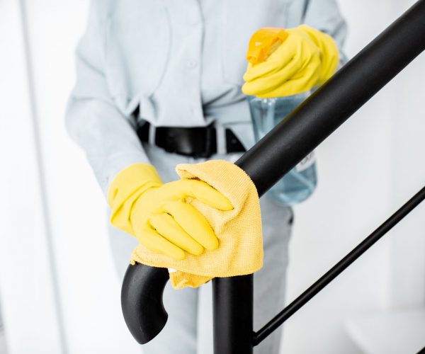Woman cleaning stair railings at home Woman in protective gloves disinfecting stair railings while cleaning at home, close-up view on hands